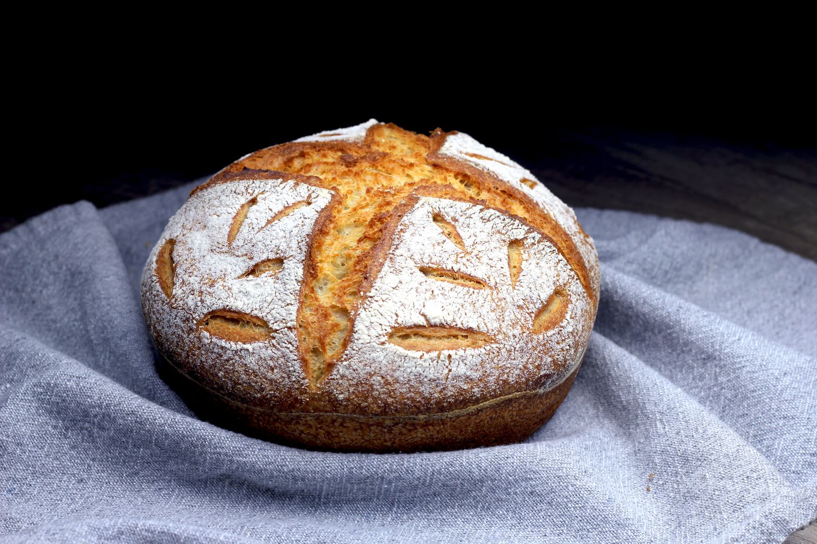 Flour-dusted round sourdough boule with leaf-pattern scoring on a linen cloth